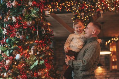 Gülümse küçük çocuk ve baba içeride Noel Baba 'yı beklerken kucaklaşıp öpüşüyorlar. Noel ağacı kış sezonunun çelenk ışıklarıyla yeni yılı kutluyoruz Noel ruhu 25 Aralık baba sevgisi arifesi