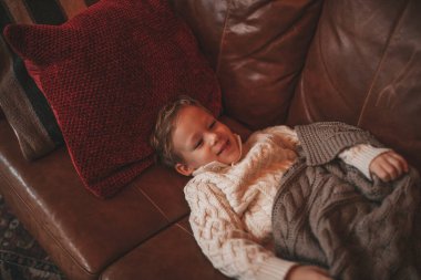 Gülümse küçük çocuk hareket halinde eğleniyor ve hayalperest mucize Noel Baba 'yı bekliyor. 25 Aralık 'ın arifesinde, kanepede örgü kıyafetli, oyuncaklarla oynayan neşeli çocuk Noel.
