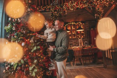 Gülümse küçük çocuk ve baba içeride Noel Baba 'yı beklerken kucaklaşıp öpüşüyorlar. Noel ağacı kış sezonunun çelenk ışıklarıyla yeni yılı kutluyoruz Noel ruhu 25 Aralık baba sevgisi arifesi