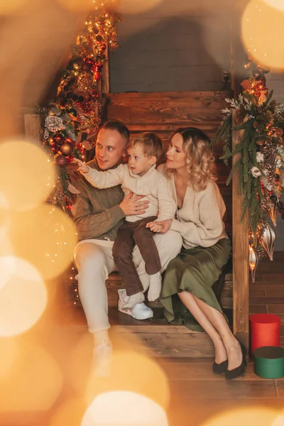 サンタ屋内を待っているニットベージュのセーターで幸せな家族の肖像画 笑顔の両親抱擁とキス彼の小さな息子Eve 12月はガーランドライトでクリスマスを祝う Noel Tree Gift Giving — ストック写真