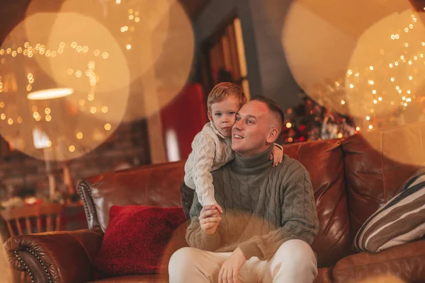 笑顔の男の子とお父さんはお互いの抱擁で楽しみ 屋内待っているサンタにキスをします ノエルの木の冬の季節のガーランドライトで新年を祝うクリスマスの精神前夜25 12月父方の愛 — ストック写真