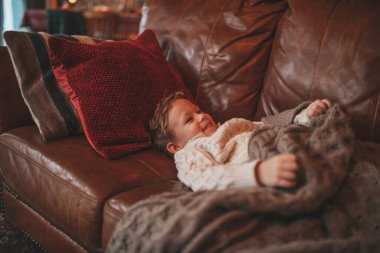 Gülümse küçük çocuk hareket halinde eğleniyor ve hayalperest mucize Noel Baba 'yı bekliyor. 25 Aralık 'ın arifesinde, kanepede örgü kıyafetli, oyuncaklarla oynayan neşeli çocuk Noel.