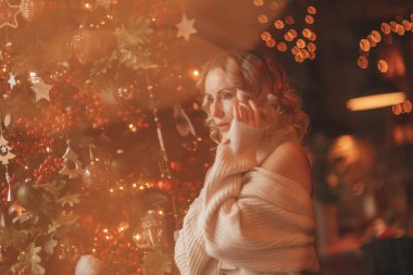 25 Aralık arifesinde Noel ağacının ışıklarının yanındaki dağ evindeki samimi, gerçek sarışın, kıvırcık saçlı hayalperestin portresi. Örgü kıyafetli bir kadın ellerini yüzüne koyuyor ve sadece Xmas 'ı kutlarken kollarına sarılıyor.