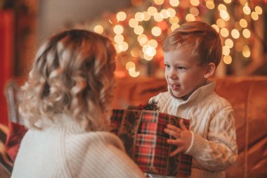 Evde Noel Baba 'yı bekleyen örgü bej kazaklı küçük oğlu olan mutlu aile babasının portresi. Anneler, 25 Aralık arifesinde Noel ağacına çelenk vererek yeni yıl hediyelerini kutlamaya bayılır.