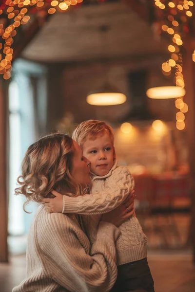 サンタ屋内を待っているニットベージュのセーターで小さな息子と幸せな家族のお母さんの肖像画 母は前夜に抱擁とキスを愛し25 12月はガーランドライトを与える新年の贈り物を祝います Noel Tree — ストック写真