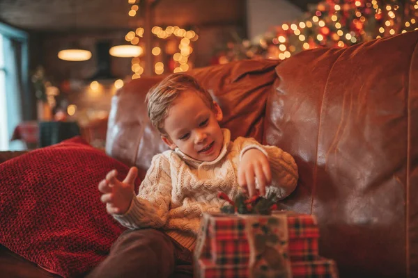 stock image Smile small child being active having fun waiting for miracle Santa open presents. Cheerful kid in casual knit outfit celebrating new year with gifts boxes garlands bokeh lights noel eve 25 december