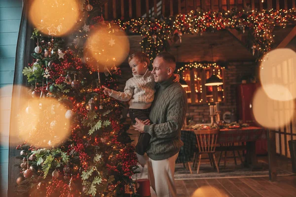 Gülümse küçük çocuk ve baba içeride Noel Baba 'yı beklerken kucaklaşıp öpüşüyorlar. Noel ağacı kış sezonunun çelenk ışıklarıyla yeni yılı kutluyoruz Noel ruhu 25 Aralık baba sevgisi arifesi