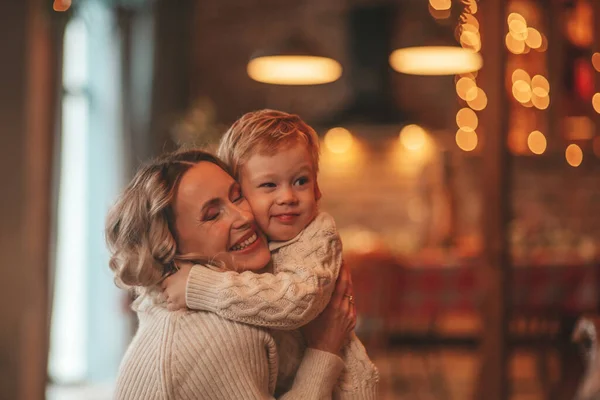 サンタ屋内を待っているニットベージュのセーターで小さな息子と幸せな家族のお母さんの肖像画 母は前夜に抱擁とキスを愛し25 12月はガーランドライトを与える新年の贈り物を祝います Noel Tree — ストック写真
