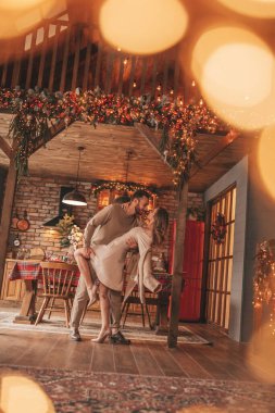 25 Aralık arifesinde evde kucaklaşan güzel bir çiftin portresi. Aşıklar gülüyor, öpücükler evde Noel 'i bekliyor. Yeni yılı kutluyoruz. Çiçek yakıyoruz. Zarif örgü kıyafetlerle süsleniyoruz.