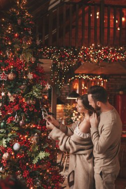 25 Aralık arifesinde evde kucaklaşan güzel bir çiftin portresi. Aşıklar gülüyor, öpücükler evde Noel 'i bekliyor. Yeni yılı kutluyoruz. Çiçek yakıyoruz. Zarif örgü kıyafetlerle süsleniyoruz.
