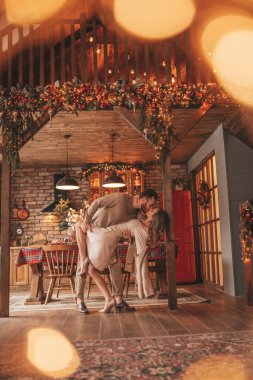 25 Aralık arifesinde evde kucaklaşan güzel bir çiftin portresi. Aşıklar gülüyor, öpücükler evde Noel 'i bekliyor. Yeni yılı kutluyoruz. Çiçek yakıyoruz. Zarif örgü kıyafetlerle süsleniyoruz.