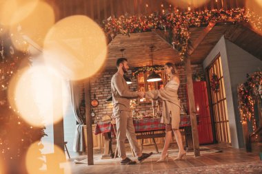 25 Aralık arifesinde evde kucaklaşan güzel bir çiftin portresi. Aşıklar gülüyor, öpücükler evde Noel 'i bekliyor. Yeni yılı kutluyoruz. Çiçek yakıyoruz. Zarif örgü kıyafetlerle süsleniyoruz.