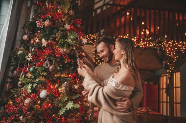 25 Aralık arifesinde evde kucaklaşan güzel bir çiftin portresi. Aşıklar gülüyor, öpücükler evde Noel 'i bekliyor. Yeni yılı kutluyoruz. Çiçek yakıyoruz. Zarif örgü kıyafetlerle süsleniyoruz.