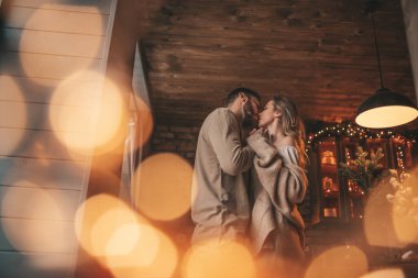 25 Aralık arifesinde evde kucaklaşan güzel bir çiftin portresi. Aşıklar gülüyor, öpücükler evde Noel 'i bekliyor. Yeni yılı kutluyoruz. Çiçek yakıyoruz. Zarif örgü kıyafetlerle süsleniyoruz.