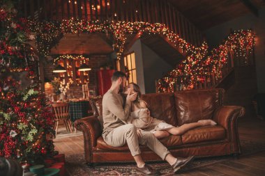 25 Aralık arifesinde evde kucaklaşan güzel bir çiftin portresi. Aşıklar gülüyor, öpücükler evde Noel 'i bekliyor. Yeni yılı kutluyoruz. Çiçek yakıyoruz. Zarif örgü kıyafetlerle süsleniyoruz.