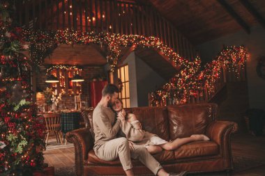 25 Aralık arifesinde evde kucaklaşan güzel bir çiftin portresi. Aşıklar gülüyor, öpücükler evde Noel 'i bekliyor. Yeni yılı kutluyoruz. Çiçek yakıyoruz. Zarif örgü kıyafetlerle süsleniyoruz.