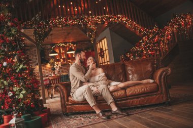 25 Aralık arifesinde evde kucaklaşan güzel bir çiftin portresi. Aşıklar gülüyor, öpücükler evde Noel 'i bekliyor. Yeni yılı kutluyoruz. Çiçek yakıyoruz. Zarif örgü kıyafetlerle süsleniyoruz.