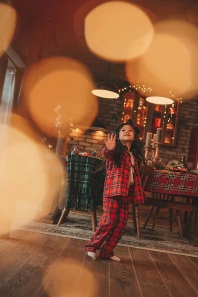 スタイリッシュな長いブルネットの髪モデルのポーズを持つアクティブな日本の子供の女の子は ボケガーランドノエルで自宅で アジアの小さなファッショニスタで赤再生Pajamaダンスジャンプ移動笑いお祝いクリスマス — ストック写真