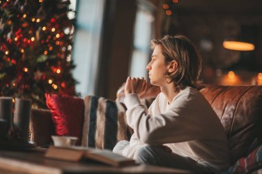 Uzun saçlı, düşünceli üzgün bakışlı, sinirli ve evde ağlayan genç bir çocuk. Şık bir zoomer olan Z jenerasyonu, yeni yıl tatilinde Noel ağacı ışıklarıyla süslenmiş 25 Aralık arifesi.