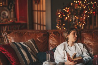 Genç, duygusal, neşeli, uzun saçlı, kahkahalar atan ve rahat evinde neşeli bir çocuk. Zoomer Z jeneratörünün keyfi yerinde. 25 Aralık arifesi Noel arifesi Noel ağacıyla Noel tatili kutlanıyor.