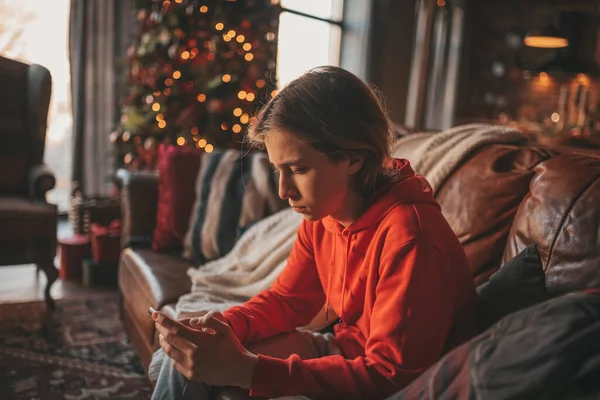 Uzun saçlı, düşünceli üzgün bakışlı, sinirli ve evde ağlayan genç bir çocuk. Şık bir zoomer olan Z jenerasyonu, yeni yıl tatilinde Noel ağacı ışıklarıyla süslenmiş 25 Aralık arifesi.