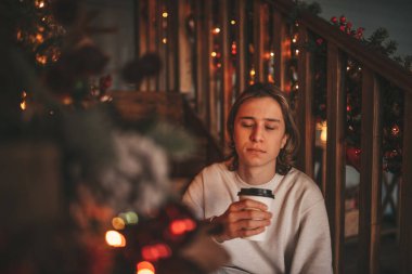 Uzun saçlı, düşünceli üzgün bakışlı, sinirli ve evde ağlayan genç bir çocuk. Şık bir zoomer olan Z jenerasyonu, yeni yıl tatilinde Noel ağacı ışıklarıyla süslenmiş 25 Aralık arifesi.