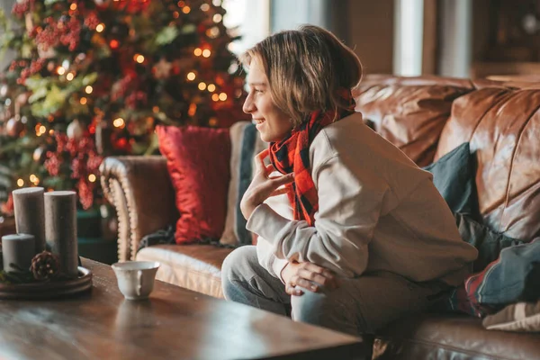 stock image Young emotional cheerful teen boy with long hair laughter and joyful at cozy home. Stylish zoomer gen Z in good mood celebrates new year holidays with xmas tree bokeh lights garlands eve 25 december