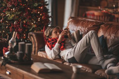 Uzun saçlı, akıllı telefon tutan genç bir çocuk. Mesajlaşmak için kablosuz teknoloji mobil cihaz kullanıyor. Zarif çocuk jenerasyonu Z, 25 Aralık arifesinde Noel 'i Noel ağacı ışıklarıyla kutluyor.