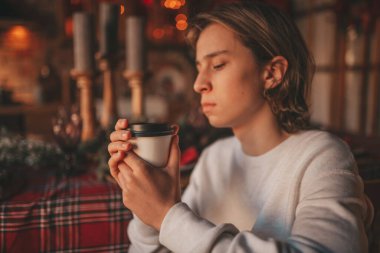 Uzun saçlı, düşünceli üzgün bakışlı, sinirli ve evde ağlayan genç bir çocuk. Şık bir zoomer olan Z jenerasyonu, yeni yıl tatilinde Noel ağacı ışıklarıyla süslenmiş 25 Aralık arifesi.