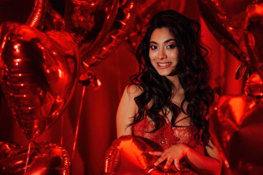 Young tempting brunette woman with perfect skin in sexy lingerie posing with heart balloons in a red room  