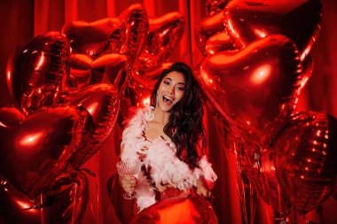 Young tempting brunette woman in sexy lace underwear and feather boa having fun with champagne on Valentine's day