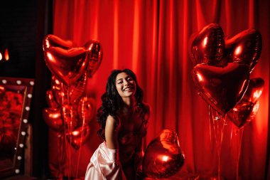 Young tempting brunette woman with perfect skin in sexy lingerie posing with heart balloons in a red room  
