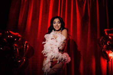 Sensual curly black hair asian woman with feather boa posing on red glamour background