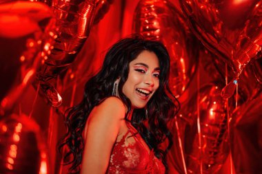 Sensual woman flirtatious temptress with curly black hair posing on red glamour background