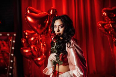 Beautiful woman wearing sexy lace underwear and a silk robe posing with roses on red glamour background 