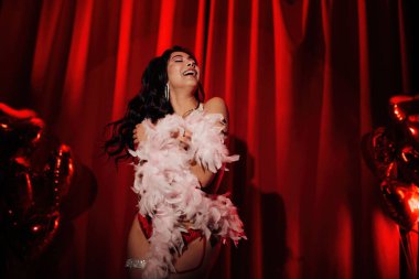 Sensual curly black hair asian woman with feather boa posing on red glamour background