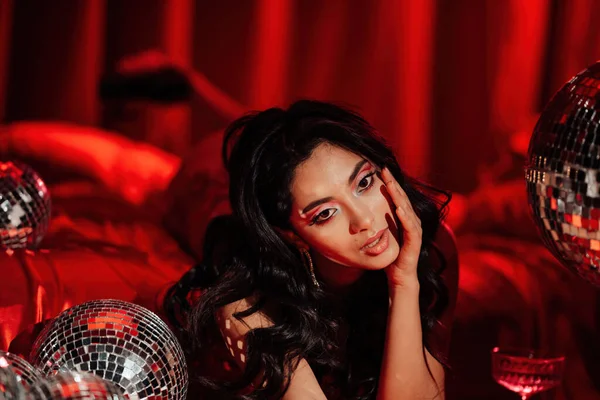Curly black hair asian model with disco balls posing in bed on Valentine's day