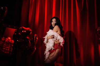 Sensual curly black hair asian woman with feather boa posing on red glamour background