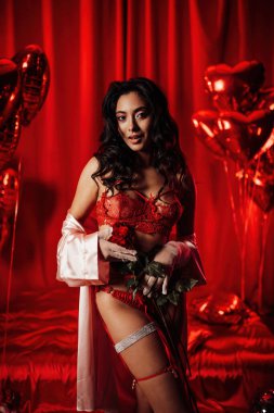 Young japanese woman wearing sexy lace underwear posing with roses on red glamour background 