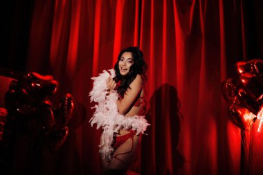 Sensual curly black hair asian woman with feather boa posing on red glamour background