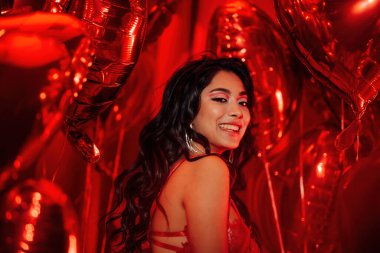 Young tempting brunette woman with perfect skin in sexy lingerie posing with heart balloons in a red room  