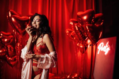 Beautiful asian black hair woman in sexy lingerie posing with cupcake in a room decorated for Valentine's Day