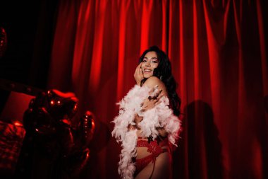 Sensual curly black hair asian woman with feather boa posing on red glamour background