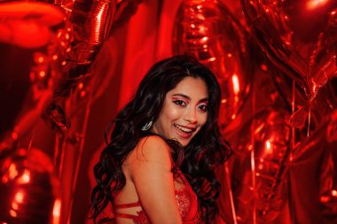 Young tempting brunette woman with perfect skin in sexy lingerie posing in bed with heart balloons