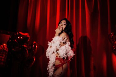 Sensual curly black hair asian woman with feather boa posing on red glamour background