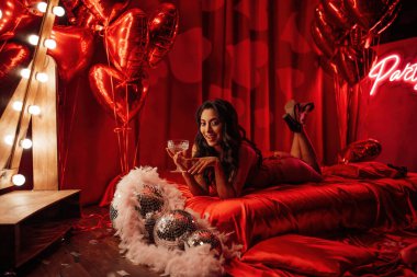 Curly black hair asian model with champagne glass posing in bed on Valentine's day