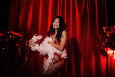 Sensual curly black hair asian woman with feather boa posing on red glamour background