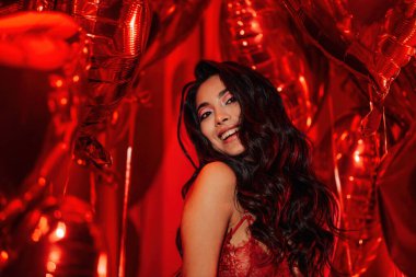 Young tempting brunette woman with perfect skin in sexy lingerie posing with heart balloons in a red room  