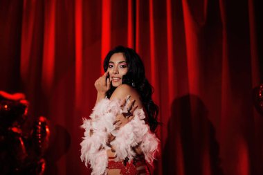 Sensual curly black hair asian woman with feather boa posing on red glamour background