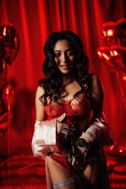 Beautiful woman wearing sexy lace underwear and a silk robe posing with roses on red glamour background 